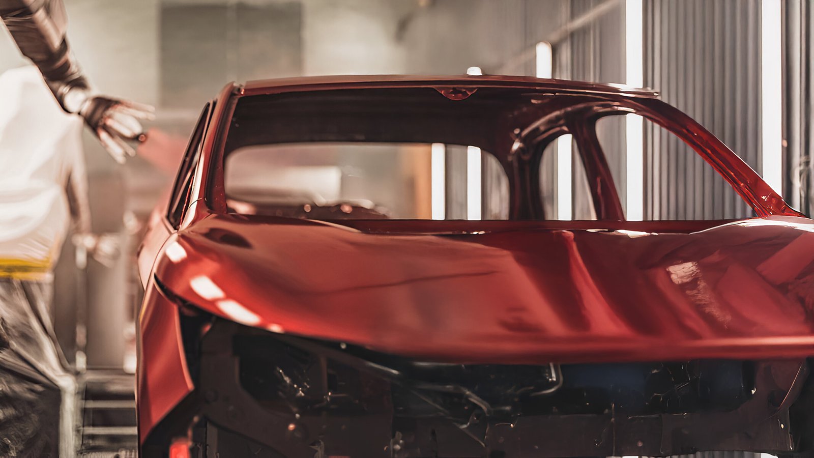 Carro recém pintado de vermelho vivo saindo de cabine de pintura numa linha robótica